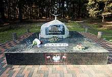 A large rock set on a pedestal of polished stone. On the pedestal, the words "Katyn Memorial" are visible. On the rock, a plaque reads "In memory of 25,000 Polish prisoners of war and professional classes who were murdered on Stalin's orders by the Soviet Secret Police in 1940 at Katyn Forest, Kharkov, Miednoye, Kozielsk, Starobielsk, Ostaszkov and elsewhere. Finally admitted in 1990 by the USSR after 50 years of shameful denial of the truth."