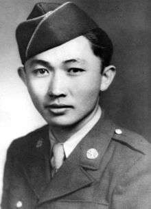 Head and shoulders of a young man looking directly at the camera and wearing a garrison cap and dark colored military jacket over a shirt and tie. The outer half of his left eyebrow is missing.