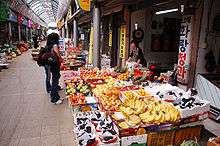 A female customer browsing a fruit shop. Banana and grapes are displayed on the front.