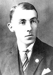 A black and white profile photograph of a young man in his late twenties, posing to the photographer and wearing a tux and a tie.