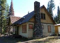 Photograph of a modest log house in a forest.