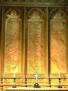 Three plaques on a wall, inscribed with the lists of the archbishops. In front of the plaques is a table with two candlesticks flanking an upright cross.