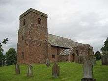 A stone church seen from the southeast with a south transept and a west tower with a plain parapet