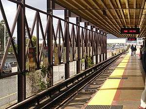 A near-empty station platform of a ground level train station. It situates next to a highway.