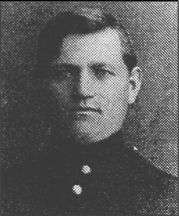 Head of a young man with thick, dark, hair parted at the side. He is wearing a military jacket with a high collar and bright buttons down the center.