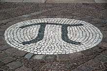 A photograph of the Greek letter pi, created as a large stone mosaic embedded in the ground.