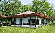 One-story building with large windows covered by white blinds and a red grid-like overhang