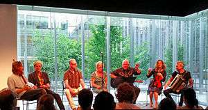 Mekons circa 2015, left to right: Lu Edmonds, Tom Greenhalgh, Steve Goulding, Sally Timms, Jon Langford, Susie Honeyman, Rico Bell (ot pictured: Sarah Corina)