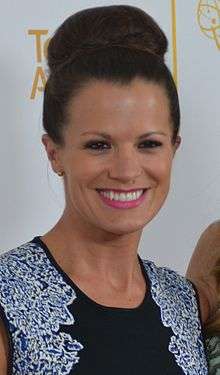 A women with brunette hair stylized in a bun, wearing a black, blue, and white outfit.