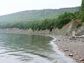 Forested mountains with rocks and pebble beach.