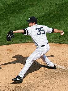 A man standing on a pitcher's mound stretches to throw a baseball from his right hand