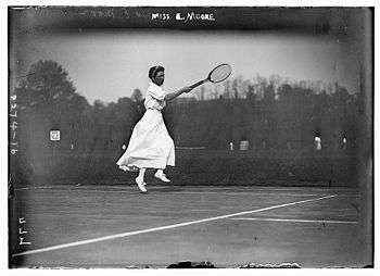 A woman in all white attire is hitting a forehand with the tennis racket in the right hand, which it is a black and white photograph