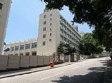 A view of a six-storey concrete school building on a steep hillside road