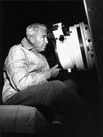 A man in his 60s looking into the eyepiece of a large telescope.