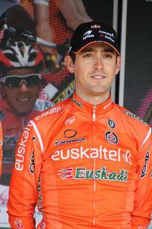 A man in his mid twenties wearing an orange cycling jersey with white and green trim, and a blasck baseball cap.