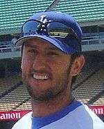 Portrait of a man wearing a blue baseball cap with "LA" on it and sunglasses over it.