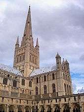 A sturdy tower with Norman details supports a delicate spire framed by four pinnacles.