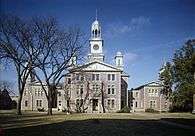 A photograph of the front of a building with a clock tower, surrounded by trees