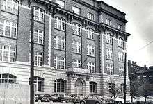 Five story brick and terra cotta building with parking lot and city street in the foreground