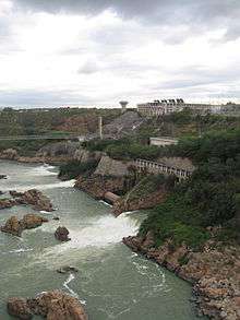 Aerial image of a coastal mountainous place with some structures located on top of it and some power lines