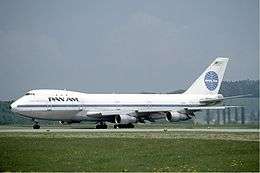 Side view of aircraft on taxiway. Grassy surfaces in foreground; hills and sky in background.