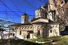 Side view of a three-domed Orthodox church with blind arches. Cliffs in the background.