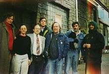 A group of seven people stand near the entrance of a  building.