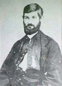 Head and shoulders of a white man with a full beard and thick hair, wearing an unbuttoned military jacket with a star-shaped medal pinned to the left breast.