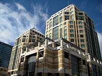 Two brown towers stand behind a blue sky with several clouds, looking from the ground