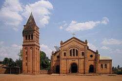 Photograph depicting the Roman Catholic parish church in Rwamagana, Eastern Province, including the main entrance, façade, the separate bell tower, and dirt forecourt