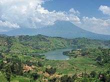 Photograph of a lake with one of the Virunga mountains behind, partially in cloud