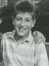 A teenage male with the hand of another resting on his left shoulder smiling for the camera