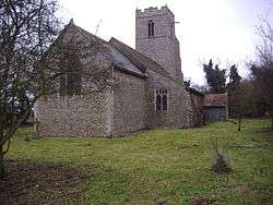 A flint church seen from the northeast showing the chancel, nave and aisle with a catslide roof, porch and battlemented tower