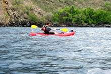 Photo of person sitting in boat with paddle. Island in background.