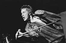 Black-and-white photo of a spiky-haired youth singing into a microphone