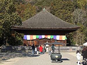 A wooden building with pyramid shaped roof. Colorful flags are hanging around the outer walls.