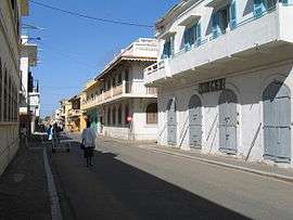 A somewhat narrow street runs straight between several lightly coloured buildings.