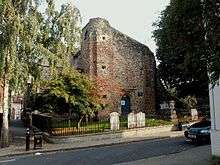 A stone tower with a sloping top, standing in a churchyard