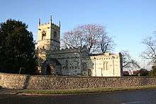 A stone church seen from the south. On the left is a tower with a battlemented parapet, in the middle is the nave, also with a battlemented parapet, and on the right is the chancel with a plain parapet