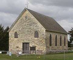 Stone buiilding, four windows along side, small window on either side of front door