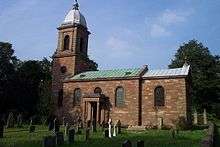 A Georgian church seen from the south.  On the left is the tower with a cupola, the nave has a circular window, two round-headed windows and a porch supported by columns, and the chancel has a single round-headed window