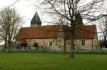 A stone church with red tiled roofs seen from the south, showing the chancel, the south aisle and porch, and the tower with a pyramidal roof