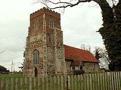 A church seen from the southwest. The body of the church and the lower part of the tower are in stone, the upper part of the tower is red brick, the south porch is timber-framed, and the roof is covered in red tiles