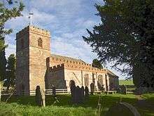 A stone church seen from the southwest with battlemented parapets on the west tower, south aisle and nave