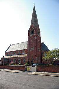 A red brick church with stone dressings, having a clerestory and a steeple