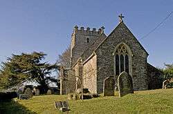 Stone building with square tower. In the foreground are gravestones.