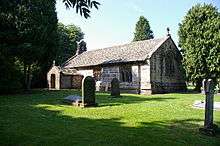 A simple low church with a south porch. On the west gable is a bellcote, and on the east gable is a cross