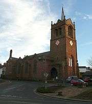 A stone church seen from the northwest with a west tower surmounted by a saddleback roof and a spirelet and a three-gabled north aisle