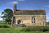 A small chapel seen from the south, with a bellcote at the left, a door and a single window