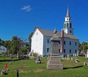 A white church, seen from the side slightly to its rear, with a cemetery in front